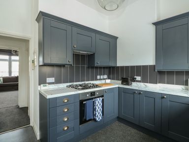A kitchen with blue cabinets a gas stove an oven a toaster and a cutting board at Northgate Ground Floor Flat in Hunstanton