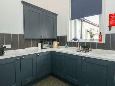 A kitchen corner with blue cabinets a sink a microwave and a window with a blue blind at Northgate Ground Floor Flat in Hunstanton
