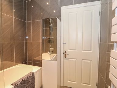 A bathroom with a bathtub a shower screen a towel on the bathtub and a white door at Northgate Ground Floor Flat Hunstanton