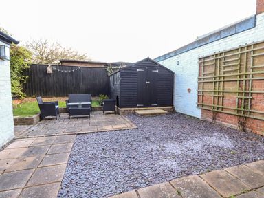 An outdoor patio area with a black storage shed black garden furniture and stone paving at Northgate Ground Floor Flat in Hunstanton
