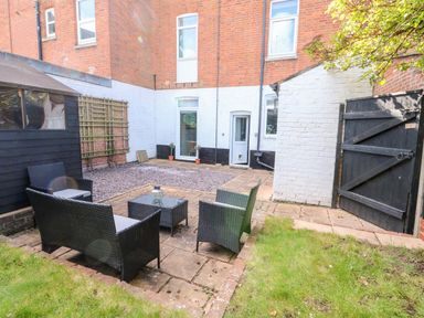 A patio area with wicker outdoor furniture and a small table next to a grass lawn at Northgate Ground Floor Flat in Hunstanton