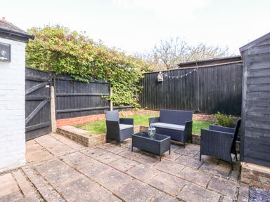 A small outdoor patio area with black wicker chairs and a table surrounded by black wooden fencing at Northgate Ground Floor Flat in Hunstanton