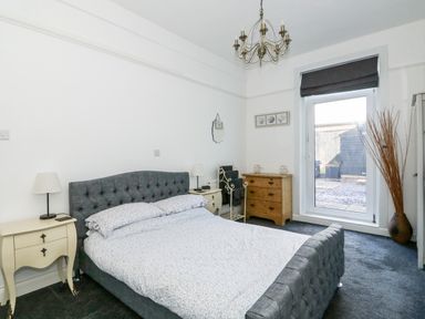 A bedroom with a double bed bedside tables lamps a wooden dresser mirror and glass door at Northgate Ground Floor Flat in Hunstanton