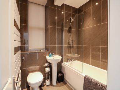 A bathroom with a toilet, pedestal sink, bathtub with shower, and a towel on the bathtub at Northgate Ground Floor Flat in Hunstanton