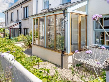 An outdoor garden area with plants a white metal bench and a glass conservatory attached to a row of houses at Sea Pickle Cottage in Llangwm Pembrokeshire