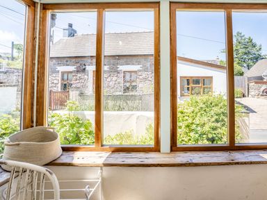 A window with wooden frames looking out to stone and white houses and greenery at Sea Pickle Cottage in Llangwm Pembrokeshire