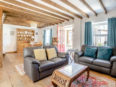 A living room with two leather sofas a wooden coffee table and a dining area with a wooden dresser at Sea Pickle Cottage in Llangwm Pembrokeshire