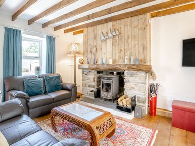 A living room with a stone fireplace and wood burner two sofas a wooden coffee table and blue curtains at Sea Pickle Cottage in Llangwm Pembrokeshire