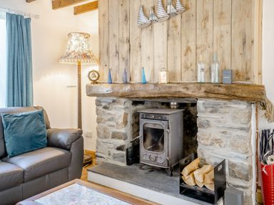 A living room with a stone fireplace wood stove log holder and a sofa with blue cushion at Sea Pickle Cottage in Llangwm Pembrokeshire