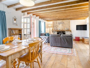A dining area with a wooden table set for four next to a living area with a fireplace sofas and a wall-mounted tv at Sea Pickle Cottage in Llangwm Pembrokeshire