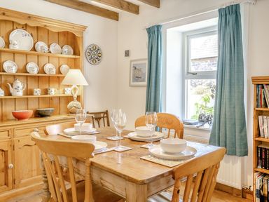 A dining room with a wooden table set with bowls and glasses and a wooden hutch with dishes at Sea Pickle Cottage in Llangwm Pembrokeshire