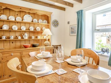 A dining area with wooden table set with bowls and glasses and a wooden cabinet with dishes at Sea Pickle Cottage in Llangwm Pembrokeshire