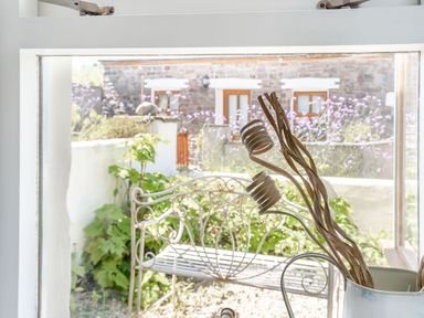 View through a window showing a metal garden bench with plants and flowers outside at Sea Pickle Cottage in Llangwm Pembrokeshire