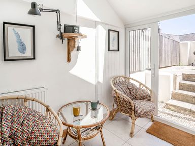 A sunlit seating area with two wicker chairs with patterned cushions a round glass table and framed leaf prints at Sea Pickle Cottage in Llangwm Pembrokeshire
