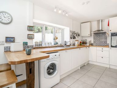 A kitchen with white cabinets wooden countertops a washing machine a stainless steel oven and hood a toaster and utensils hanging on the wall at Sea Pickle Cottage in Llangwm Pembrokeshire
