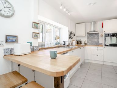 A kitchen with white cabinets wooden countertops a tiled floor and a clock on the wall at Sea Pickle Cottage in Llangwm Pembrokeshire