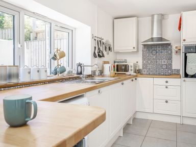 A kitchen with white cabinets wooden countertops and patterned tile backsplash at Sea Pickle Cottage in Llangwm Pembrokeshire