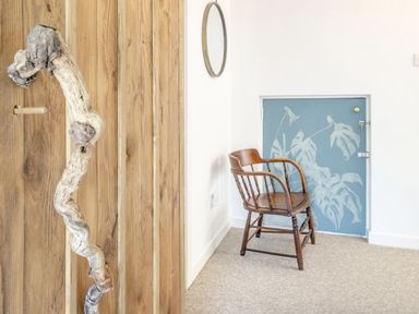 A wooden chair next to a blue door with white leaf designs and a round mirror on a white wall in a room at Sea Pickle Cottage in Llangwm Pembrokeshire