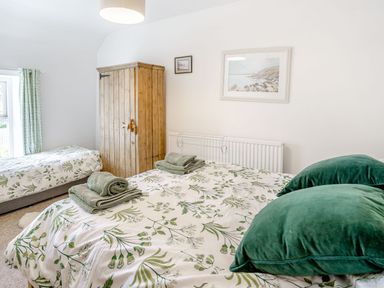 A bedroom with two beds a wooden wardrobe and artwork on the wall at Sea Pickle Cottage in Llangwm Pembrokeshire