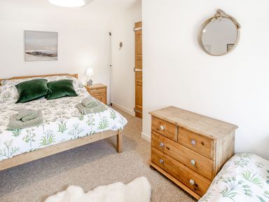 A bedroom with a wooden bed and green pillows a wooden chest of drawers a round wall mirror and a bedside table with a lamp at Sea Pickle Cottage in Llangwm Pembrokeshire