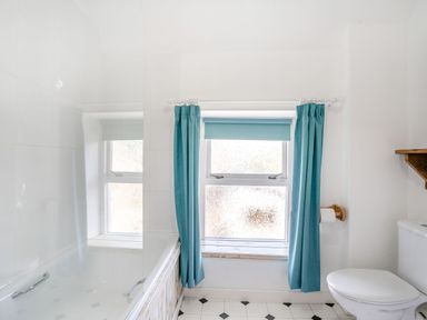 A bathroom with a bathtub and a toilet next to a window with blue curtains at Sea Pickle Cottage in Llangwm Pembrokeshire