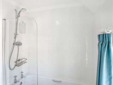 A bathroom with a bathtub shower combination blue shower curtain and white tiled walls at Sea Pickle Cottage in Llangwm Pembrokeshire