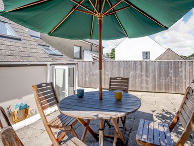 A patio with a round wooden table and four wooden chairs under a green umbrella at Sea Pickle Cottage in Llangwm Pembrokeshire