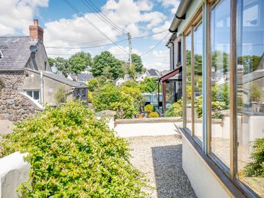 A garden area with green bushes gravel path and a building with large windows at Sea Pickle Cottage in Llangwm Pembrokeshire