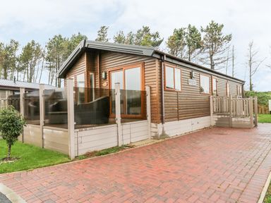 An exterior view of a wooden cabin with glass patio enclosure and a brick driveway at Huckleberry in Runswick Bay near Staithes