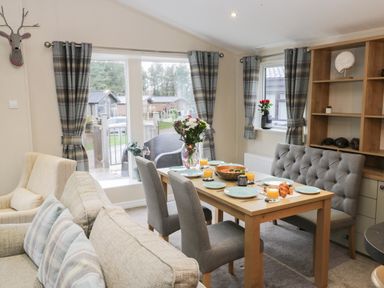 A dining area with a wooden table set with plates and glasses of orange juice next to a sofa and armchair at Huckleberry in Runswick Bay near Staithes
