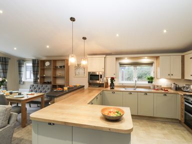 A kitchen and dining area with wooden countertops a dining table and chairs a fruit bowl and pendant lights at Huckleberry in Runswick Bay near Staithes