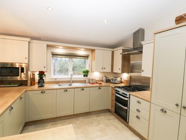 A kitchen with beige cabinets a wooden countertop a stainless steel oven and microwave a sink under a window and kitchen appliances at Huckleberry Runswick Bay near Staithes
