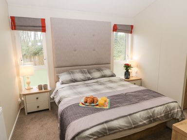 A bedroom with a double bed with plaid bedding two bedside tables with lamps and a tray with croissants and orange juice on the bed at Huckleberry in Runswick Bay near Staithes