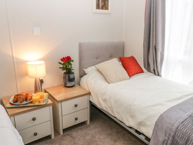 A bedroom with two beds side by side two bedside tables with a lamp flowers and a tray with croissants and orange juice at Huckleberry in Runswick Bay near Staithes