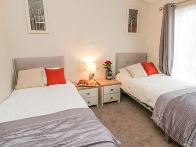 A bedroom with two single beds separated by two nightstands with a lamp flowers and tray with croissants and juice at Huckleberry in Runswick Bay near Staithes