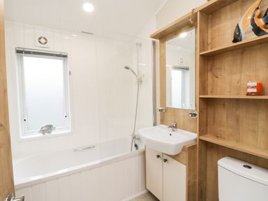 A bathroom with a bathtub shower sink toilet and wooden shelves at Huckleberry in Runswick Bay near Staithes