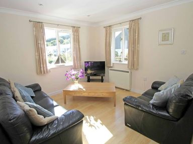 A living room with two black leather sofas a wooden coffee table with flowers and a television at Waters Edge in Falmouth