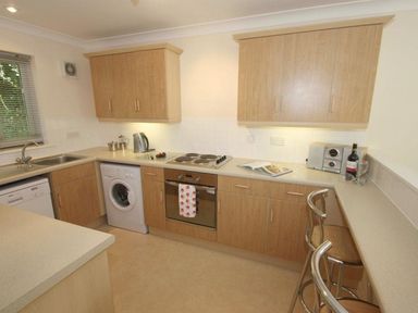 A kitchen with wooden cabinets a washing machine an oven a stovetop a sink and two bar stools at Waters Edge in Falmouth