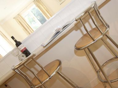 A kitchen counter with two metal bar stools a bottle of wine two wine glasses and an open book at Waters Edge in Falmouth