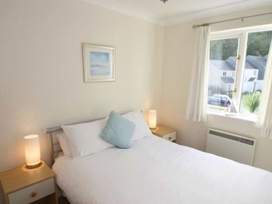 A bedroom with a bed between two bedside tables with lamps and a window in the corner at Waters Edge in Falmouth