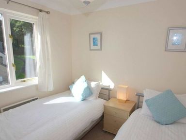 A bedroom with two single beds a wooden nightstand with a lamp and two framed pictures on the wall at Waters Edge in Falmouth