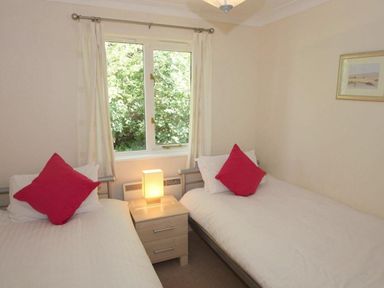 A bedroom with two single beds a nightstand with a lamp and a window with curtains at Waters Edge in Falmouth