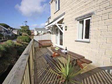A wooden balcony with outdoor table bench seating and a wooden bench attached to a stone house at Waters Edge in Falmouth
