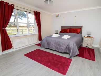 A bedroom with a bed with gray bedding and red pillows red curtains and rugs and two bedside tables at Glyn Cottage in Llanon