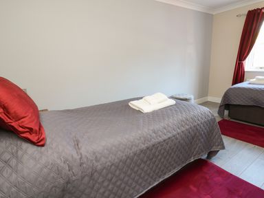A bedroom with two single beds covered with gray quilts and red pillows at Glyn Cottage in Llanon