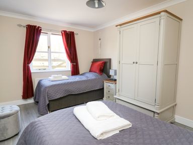A bedroom with two beds covered with gray bedspreads and white towels on them a white wardrobe red curtains and a window at Glyn Cottage in Llanon