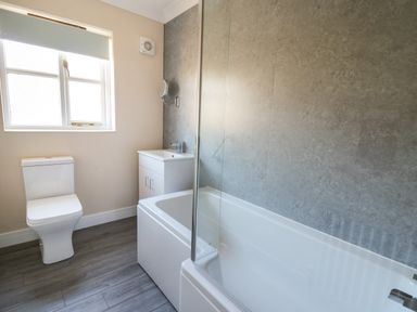 A bathroom with a toilet, sink, bathtub with glass screen, and a window at Glyn Cottage in Llanon