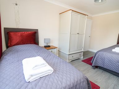 A bedroom with two single beds gray bedspreads red pillows white wardrobe and a bedside table at Glyn Cottage in Llanon