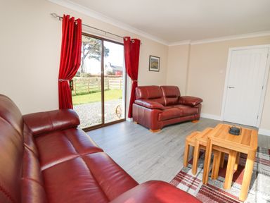 A living room with red leather sofas wooden nesting tables and red curtains at Glyn Cottage in Llanon