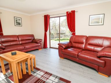 A living room with two red leather sofas a stack of wooden nesting tables and red curtains at Glyn Cottage in Llanon